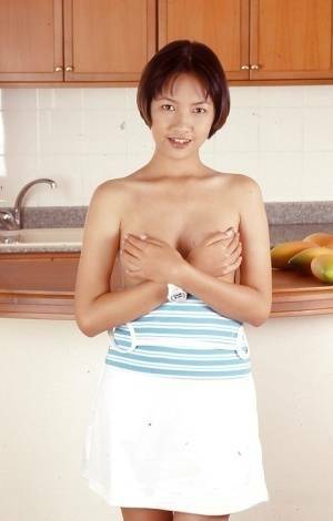 Clothed Asian with tiny tits is posing in the kitchen with spread legs on fansgirls.net