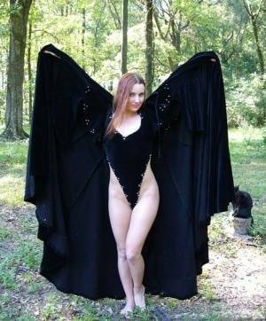 Redhead amateur Amber Lily models nude in a forest draped in a black cape on fansgirls.net