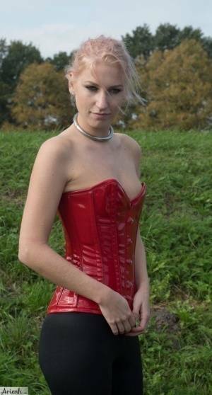 Collared girl Arienh Autumn models a red leather corset while in a field on fansgirls.net