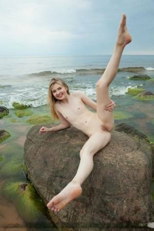 Slim teen Nimfa removes a black bikini to pose naked on seaside rocks on fansgirls.net