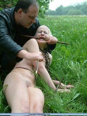 Naked blonde slave is caned and stomped on in a field of lush grass on fansgirls.net