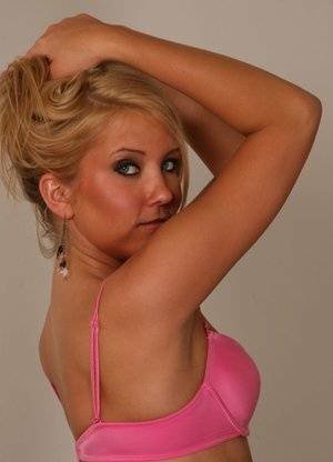 Blonde amateur Jocalynn piles up her hair before getting naked on a bed on fansgirls.net