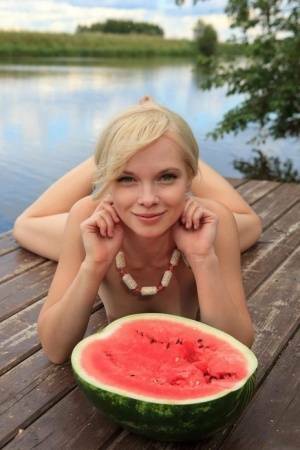 Beautiful blonde Feeona eats a watermelon while posing naked on lakeside dock on fansgirls.net